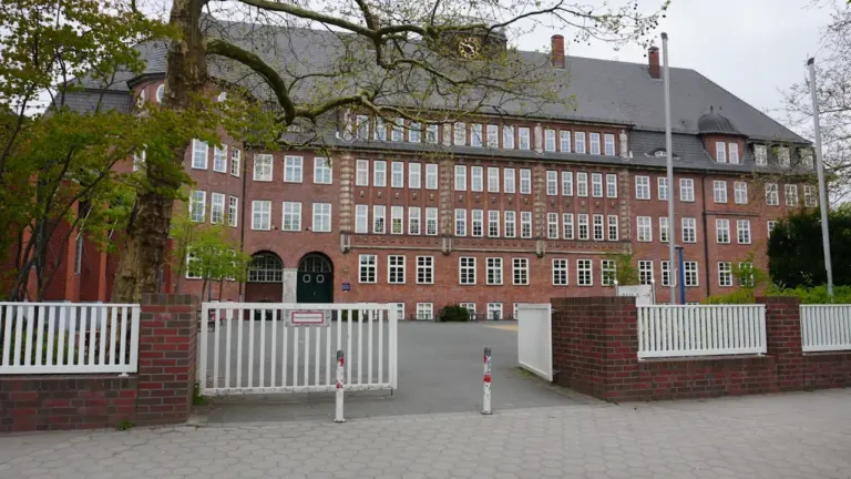 Ein historisches Ziegelgebäude mit offenem Tor und Bäumen im Vordergrund.