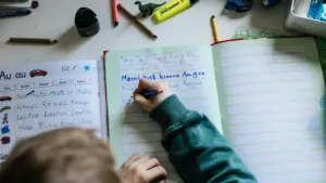 Ein Kind schreibt konzentriert mit einem Stift in ein deutsches Schulheft.