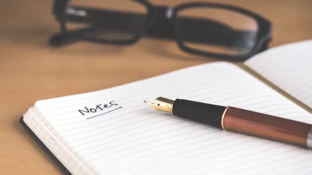 Ein Füllfederhalter liegt auf einem Notizbuch mit der Aufschrift Notes neben einer Lesebrille.