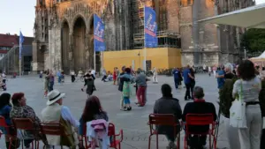 Menschen tanzen Tango auf einem Platz vor einer gotischen Kathedrale bei Abendlicht.