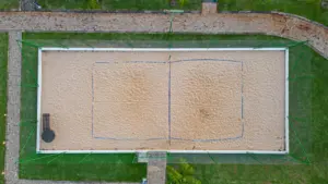 Luftaufnahme eines leeren Beach-Tennisplatzes mit Sandboden und umlaufendem Sicherheitsnetz.