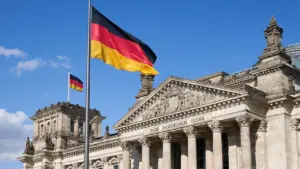 Deutscher Reichstag in Berlin mit wehender deutscher Flagge vor blauem Himmel.