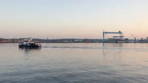 Ein kleines Boot fährt auf der Kieler Förde vor der Industriekulisse bei Sonnenuntergang.
