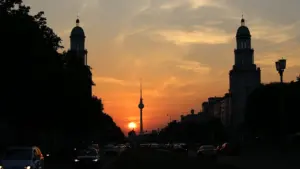 Blick über eine Berliner Straße auf den Fernsehturm während eines stimmungsvollen Sonnenuntergangs.