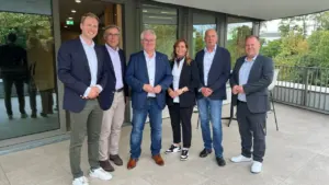 Sechs Personen stehen nebeneinander für ein Gruppenfoto auf einer modernen Terrasse vor einem Bürogebäude.