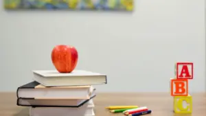 Ein roter Apfel liegt auf einem Stapel Schulbücher neben ABC-Holzklötzen auf einem Schreibtisch.