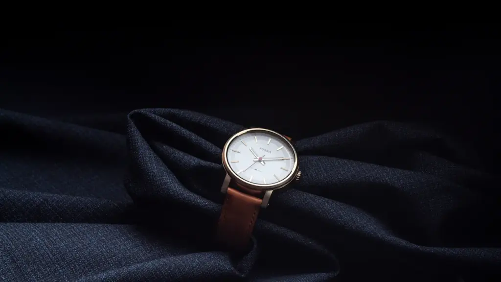 Analoge Armbanduhr mit braunem Lederarmband auf dunklem, elegantem Stoff arrangiert.