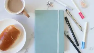 Ein Notizbuch, Kaffee und Gebäck auf einem Marmortisch für achtsame Tagesplanung und Reflexion.