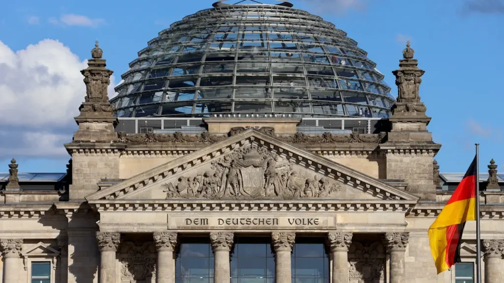 Das Reichstagsgebäude mit Glaskuppel und deutscher Flagge unter blauem Himmel in Berlin.