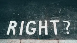 Das Wort 'RIGHT?' in weißen Buchstaben auf grauem Asphalt, eine kritische Hinterfragung von Entscheidungen.