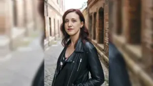 Eine Frau mit rötlichem Haar trägt eine schwarze Lederjacke in einer alten Backsteingasse.