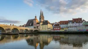 Blick auf die Regensburger Altstadt mit Kathedrale und Steinbrücke über die Donau bei Sonnenuntergang.