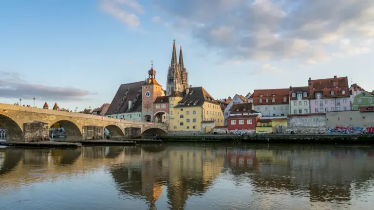 Blick auf die Regensburger Altstadt mit Kathedrale und Steinbrücke über die Donau bei Sonnenuntergang.