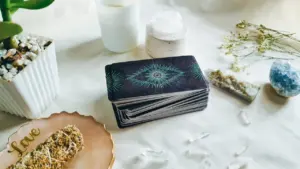 Ein Set Tarotkarten neben einer weißen Kerze und Kristallen auf hellem Untergrund.