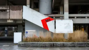 Brutalistisches Gebäude in Essen mit rotem Hinweisschild und Trockengräsern im Vordergrund.