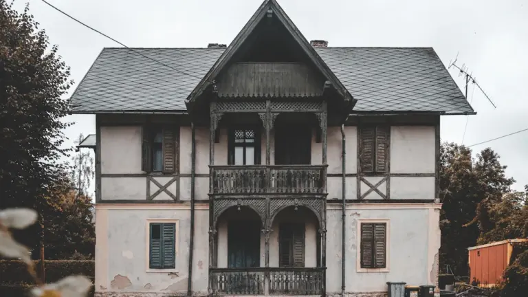 Ein altes, verlassenes zweistöckiges Haus mit Balkon in einer ländlichen Umgebung.