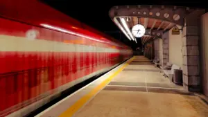 Ein roter Zug fährt in der Nacht an einem leeren Bahnsteig vorbei.