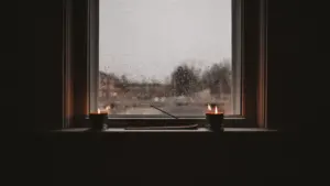 Ein gemütliches Fenster mit brennenden Kerzen während eines verregneten Tages.