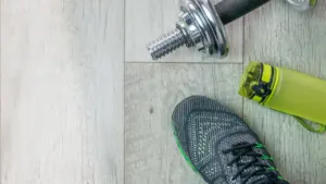 Fitness-Ausrüstung mit Turnschuhen, Hantel und einer Trinkflasche auf einem hölzernen Boden.