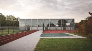 Moderne Sporthallenarchitektur in Deutschland mit Außenanlagen und Laufbahn bei Sonnenaufgang.