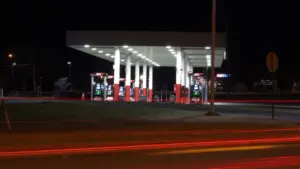 Eine beleuchtete Tankstelle bei Nacht mit vorbeifahrenden Autos auf einer Landstraße.