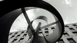 Abstrakte kinetische Metallskulptur vor einem modernen Gebäude, aufgenommen in Schwarz-Weiß-Optik.